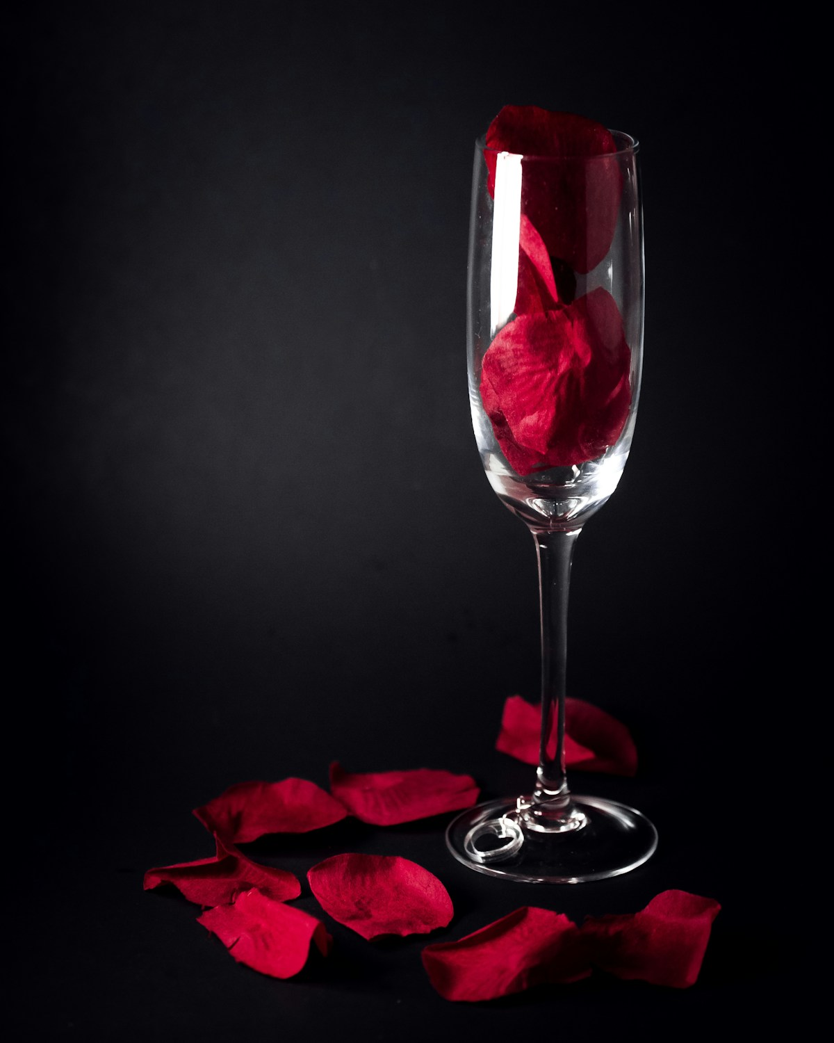 Pétales de roses rouges dans une flûte sur fond noir