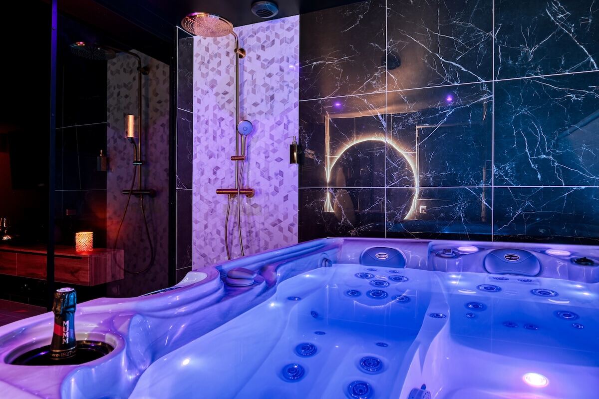 Jacuzzi privatif illuminé de bleu dans une salle de bain en marbre noir